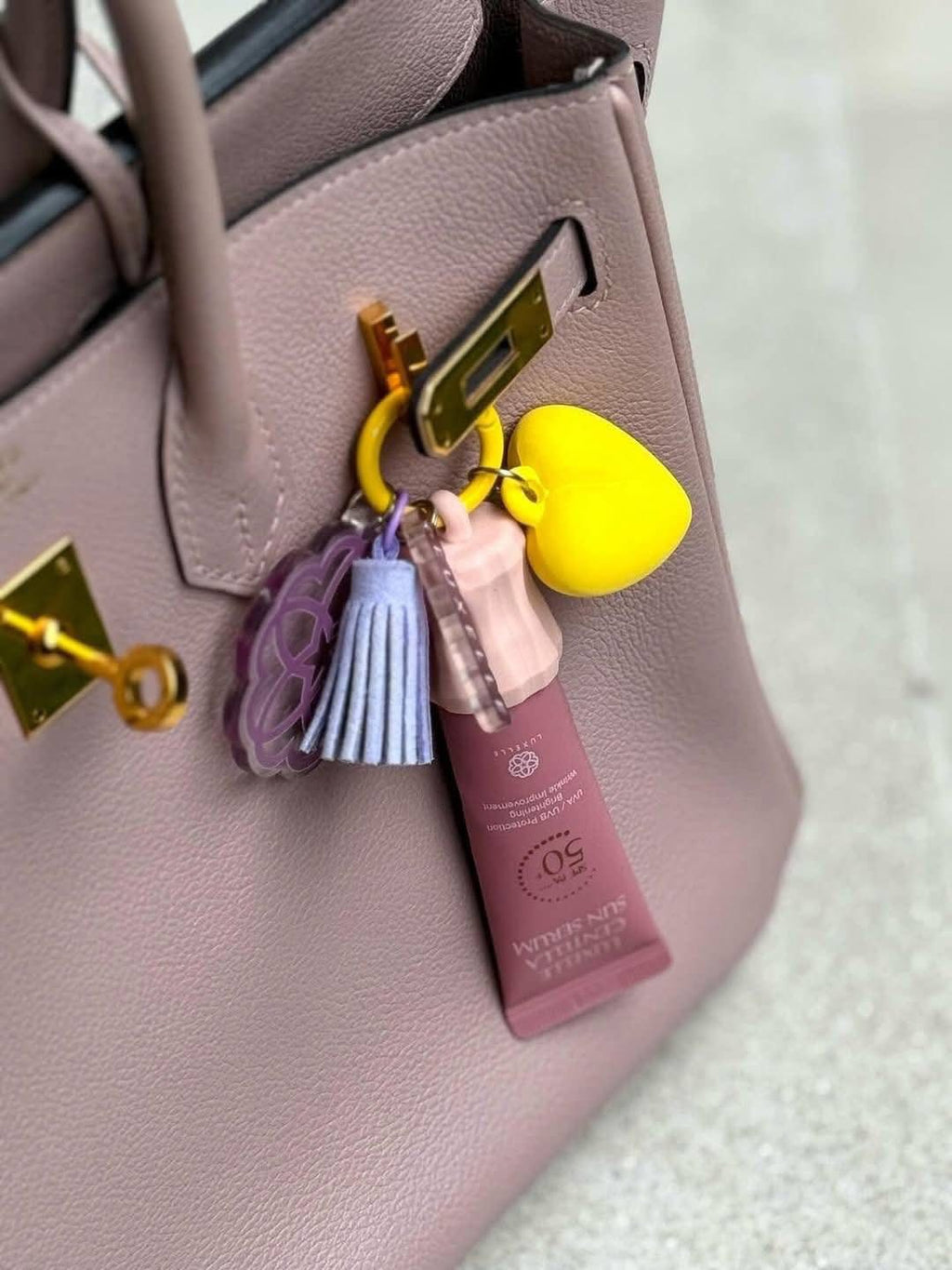 Keychain with heart, tassel, and bottle charm attached to a pink handbag.