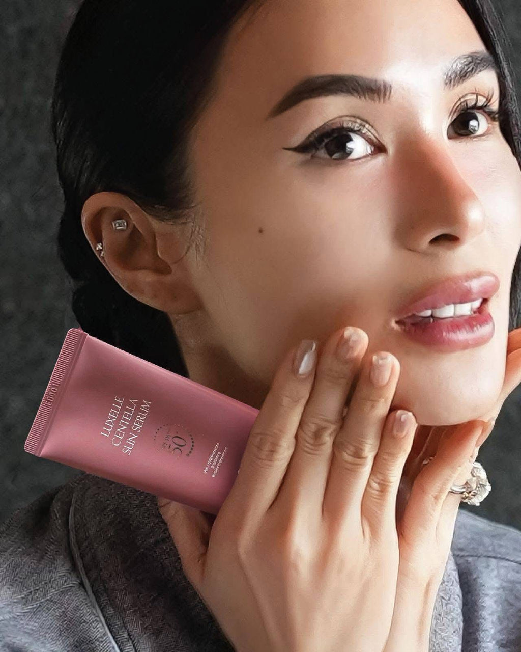 Woman holding a pink sunscreen tube close to her face against a dark background