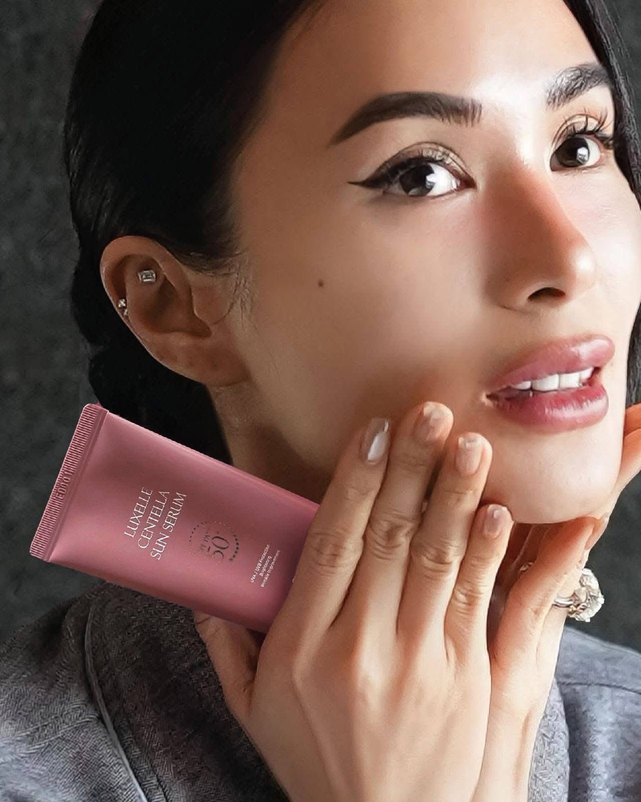 Woman holding a pink sunscreen tube close to her face against a dark background