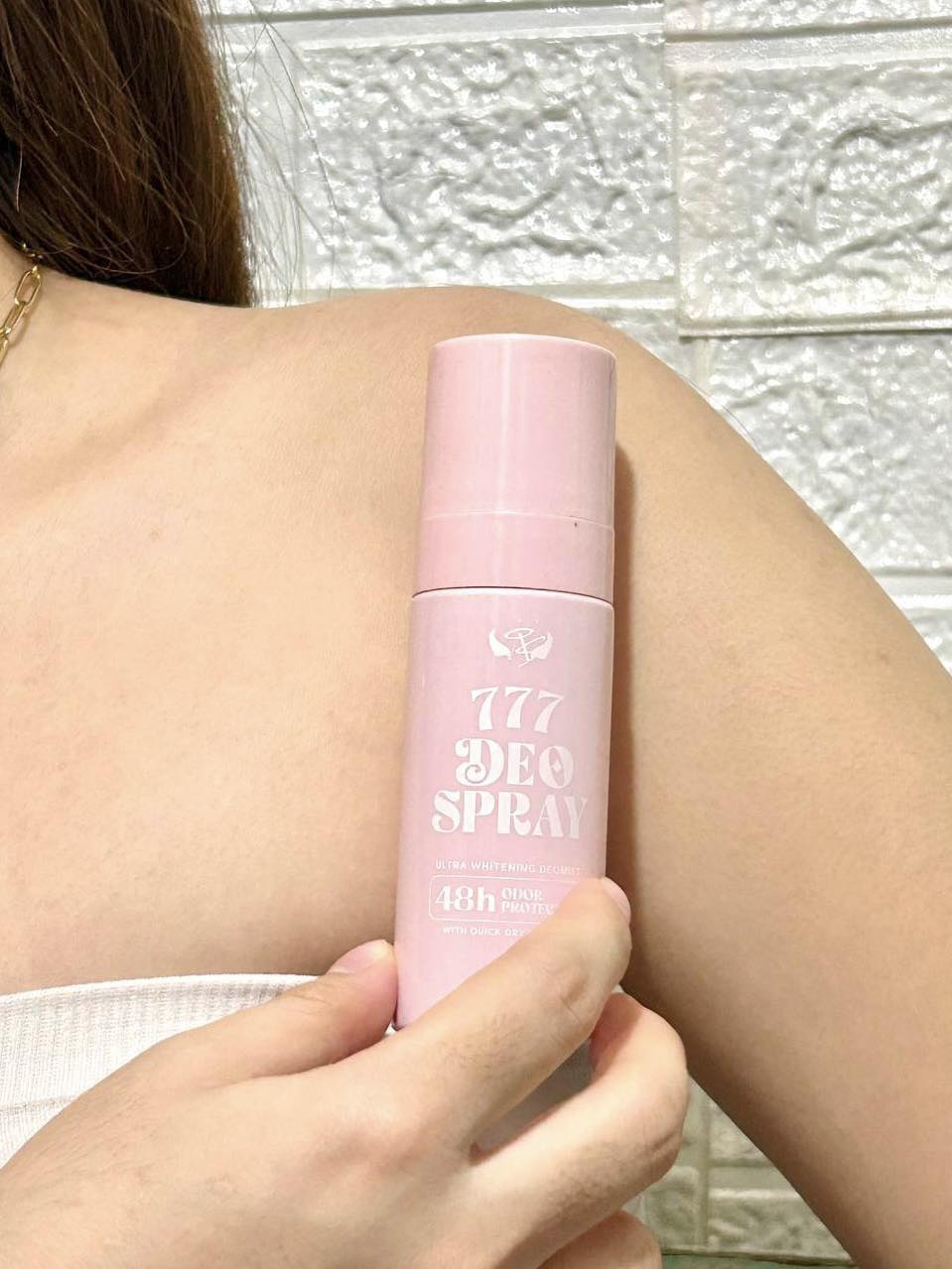Whitening underarm for chicken skin Person holding a pink deodorant spray can against a textured wall.