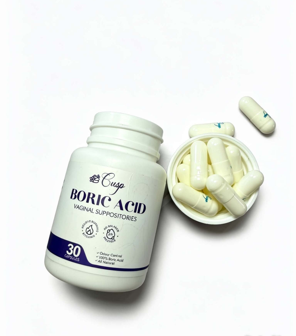 A white plastic bottle of Cusgo Boric Acid vaginal suppositories next to a small dish filled with off-white capsules, with one capsule lying nearby on a clean white background.