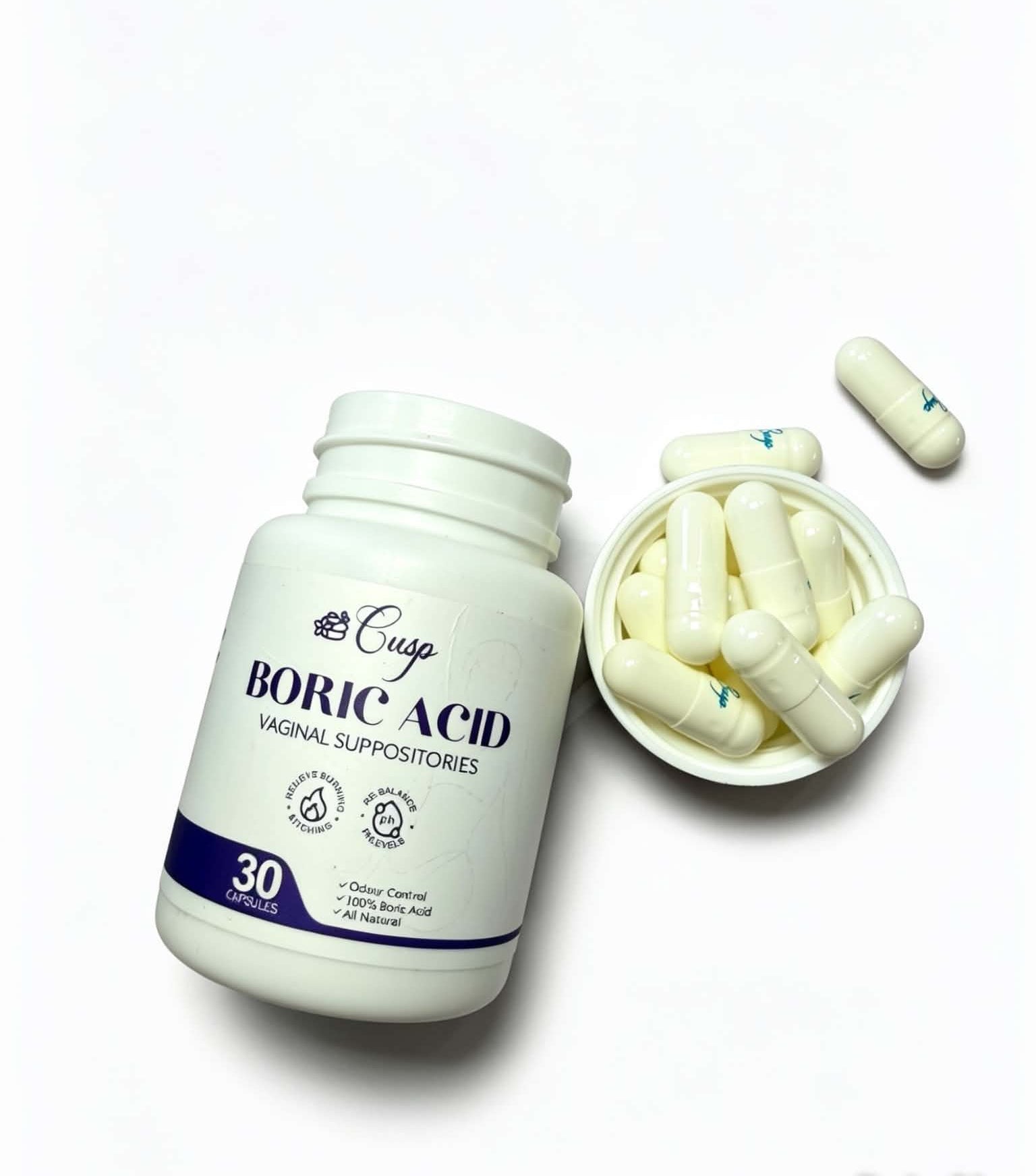 A white plastic bottle of Cusgo Boric Acid vaginal suppositories next to a small dish filled with off-white capsules, with one capsule lying nearby on a clean white background.